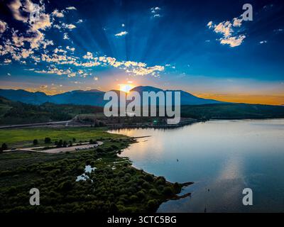 Aus der Vogelperspektive ziehen sich die strahlenden Finger der Sonne über den Himmel und illustrieren den ruhigen See und die zerklüfteten Gipfel der Berge in Aspen, Colorado, USA. Stockfoto