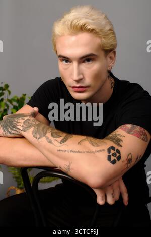 Ein stilvoller blonder Teenager zeigt selbstbewusst farbenfrohe Tattoos und setzt sich für die Jugendkultur ein. Stockfoto