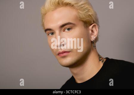 Ein selbstbewusster Teenager zeigt seine auffälligen Details und seinen trendigen Stil vor einem schlichten Hintergrund. Stockfoto