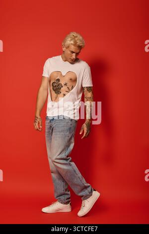 Ein stilvoller junger Mann mit trendigen Tattoos steht selbstbewusst in Freizeitkleidung und verkörpert die Jugendkultur. Stockfoto