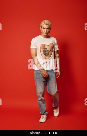 Ein hübscher Teenager in lässiger Kleidung steht selbstbewusst mit einem auffälligen roten Hintergrund. Stockfoto