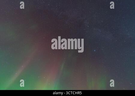 Eine atemberaubende Langzeitaufnahme der leuchtend grünen und roten Aurora Borealis oder Polarlichter, die über den sternenklaren Nachthimmel tanzen. Stockfoto