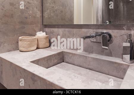 Moderner Kosmetikbereich im Bad mit Natursteinbecken, Holzregal und Spiegel. Ein Haartrockner hängt in der Nähe, was eine vollständige Ausstattung vorschlägt Stockfoto