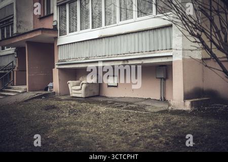 Ein Stoffstuhl steht vor dem Appartementgebäude. Den Sperrmüll aus einer Wohnung wegwerfen Stockfoto