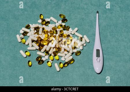 Medizinisches Stillleben: Thermometer, gelbe und weiße Kapseln liegen auf grünem Hintergrund und symbolisieren Gesundheit und Behandlung in einer klinischen Umgebung Stockfoto