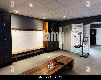Salford, Großbritannien - 25. September 2025: Ruhiger Umkleideraum mit Holzbänken, Schließfächern, weißen Fliesenwänden und einem Werbestand. Stockfoto