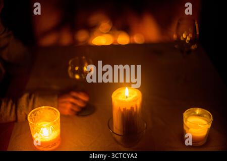 Eine Person genießt ein Glas Wein neben Kerzen und einem flackernden Kamin, was eine Atmosphäre der Wärme und Ruhe im sanft beleuchteten Raum schafft. Stockfoto