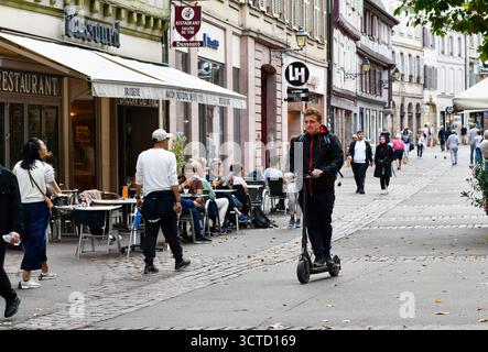 Junger Mann, der auf einer Straße in Colmar im Elsass in Frankreich mit Elektroroller fährt. Stockfoto
