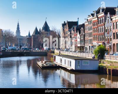 Amsterdamer Kanal mit Hausboot und Montelbaanstoren - Klassischer Blick auf einen Amsterdamer Kanal mit einem Hausboot im Vordergrund, historischem Giebelhous Stockfoto