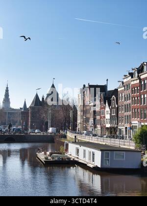 Amsterdamer Kanal mit Hausboot und Montelbaanstoren - Klassischer Blick auf einen Amsterdamer Kanal mit einem Hausboot im Vordergrund, historischem Giebelhous Stockfoto