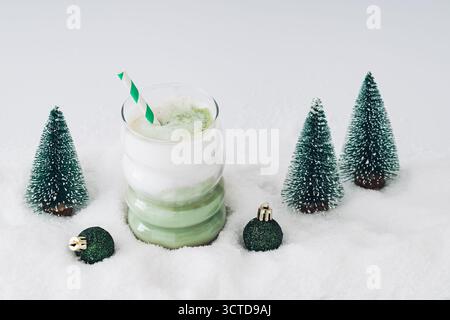 Weihnachtskomposition mit Matcha Latte und Weihnachtsbäumen und Dekorationen auf schneebedecktem Hintergrund. Minimales Weihnachts- und Neujahrskonzept. Stockfoto