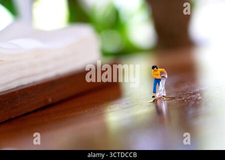 Die Miniaturfigur gießt Wasser auf eine reflektierende Holzoberfläche und verbindet spielerische Kreativität mit fantasievollen Geschichten in einer skurrilen Makroszene. Stockfoto