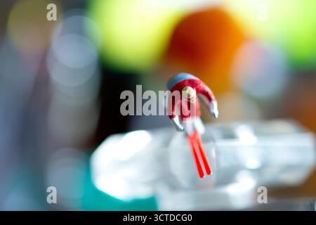 Eine Miniatur-Skifahrerfigur scheint mitten im Sprung durch einen farbenfrohen, abstrakten Hintergrund zu schweben und eine surreale, dynamische Szene zu erschaffen. Stockfoto