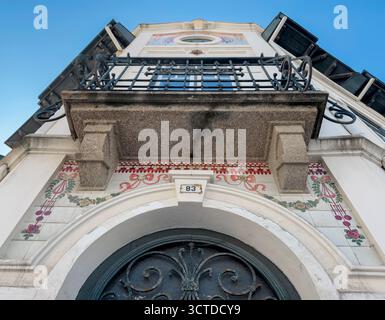 Nahaufnahme einer dekorativen Gebäudefassade in Portugal mit kunstvoll verziertem schmiedeeisernen Balkon, bogenförmigem Eingang und traditioneller Keramikfliese Stockfoto