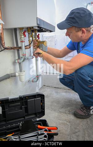 Mann, der einen neuen Kessel installiert, Heizungsrohre angeschlossen und an der Rohrleitung arbeitet. Stockfoto