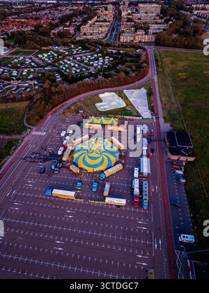 Aus der Vogelperspektive des Zirkus auf dem Parkplatz neben dem Skatepark und der Wohnzone, gelb-blaues Zelt, Anhänger und Rampen stehen im Kontrast zu gedämpften Stadttönen Stockfoto