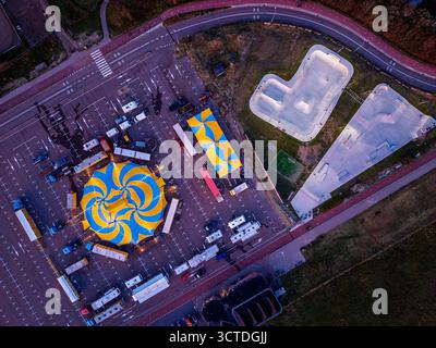 Aus der Vogelperspektive des Zirkus auf dem Parkplatz neben dem Skatepark und der Wohnzone, gelb-blaues Zelt, Anhänger und Rampen stehen im Kontrast zu gedämpften Stadttönen Stockfoto