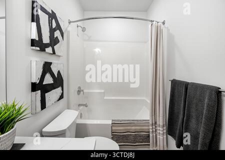 Badezimmer mit weißer Toilette und schwarz-weißem Duschvorhang. Der Duschvorhang hängt über der Wanne Stockfoto