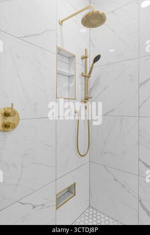 Der goldfarbene Duschkopf ist an einer weißen Wand montiert. Der Duschkopf ist an einem goldenen Rohr befestigt Stockfoto