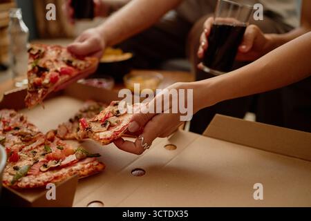 Junge Erwachsene Mann und Frau teilen sich Pizza und trinken Soda drinnen Stockfoto