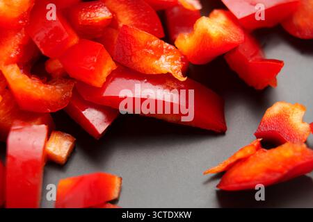 Stücke gehackter frischer roter Paprika auf schwarzer Keramik. Bio-Gemüsesalat-Zutat. Makroaufnahme. Stockfoto
