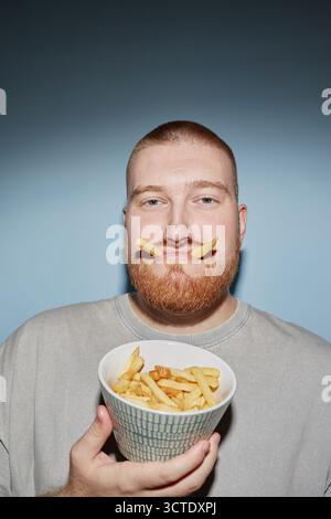 Porträt eines jungen Erwachsenen, der Pommes frites hält und lustiges Gesicht macht Stockfoto