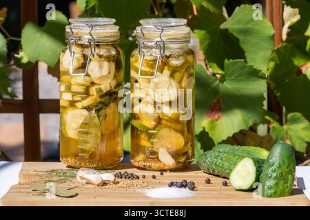 Hausgemachte eingelegte Gurkenscheiben im Glasgefäß auf hölzernem Schneidebrett mit Gewürzen; Dill-Gurken und Zutaten in der Outdoor-Szene Stockfoto