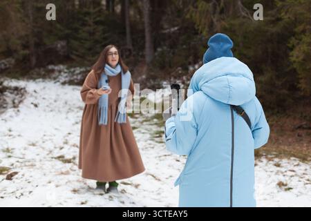 Zwei Bloggerinnen haben Spaß in einer Winterlandschaft. Eine trägt einen braunen Mantel und Schal während des Gesprächs, während die andere in einem blauen Mantel sie benutzt Stockfoto