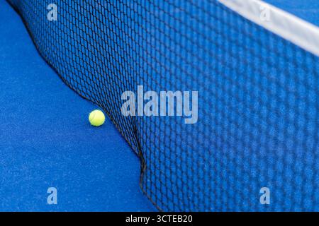 Gelber Ball auf dem Boden hinter dem Paddle oder Tennisnetz auf dem blauen Platz im Freien oder drinnen. Tennis- oder Padel-Platz Stockfoto