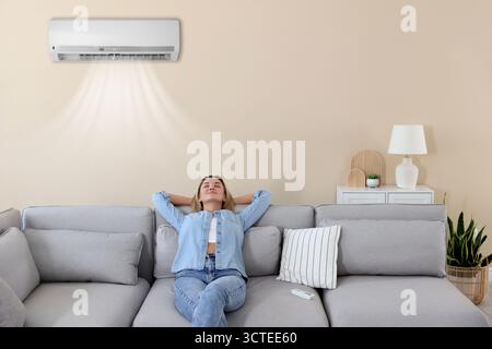 Frau, die sich unter der Klimaanlage auf dem Sofa zu Hause entspannt Stockfoto
