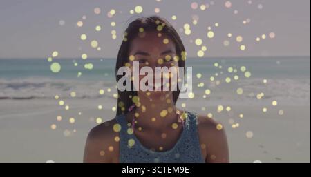 Lächelnde Frau in blauem Häkelkleid über rosa Badeanzug, die am Strand steht, mit goldenen Bokeh-Effekten Stockfoto