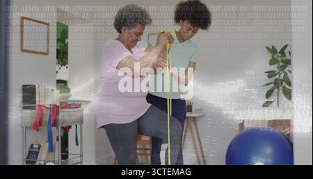 Physiotherapeut hilft Senioren beim Balancieren auf einem Fuß mit gelbem Resistenzband im Reha-Raum Stockfoto