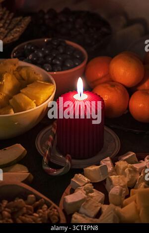 Ein warmer Feiertagstisch mit einer roten Kerze, Mandarinen, Nüssen und Süßigkeiten. Gemütliches festliches Stillleben in Deutschland. Stockfoto