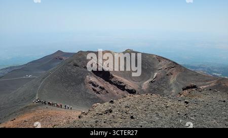 Eine Gruppe von Wanderern folgt einem Pfad entlang des Randes eines ausgedehnten, ruhenden Vulkankraters auf dem Ätna in Sizilien, Italien. Stockfoto