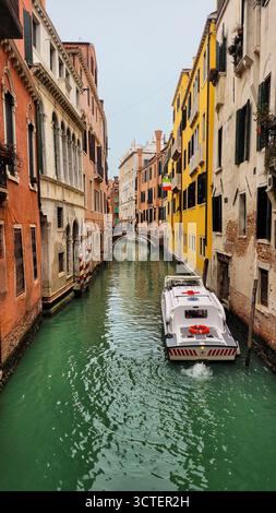Ein klassischer und stimmungsvoller Blick auf Venedig, Italien, während ein Sanitäter-Boot einen schmalen Kanal mit farbenfrohen, historischen Gebäuden befährt. Stockfoto