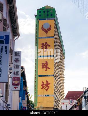 Singapur, Singapur - 9. April 2024: Blick auf das pulsierende Gebäude des People's Park Complex, dessen gelbe Fassade mit roten chinesischen Schriftzeichen vor dem weichen Himmel steht. Stockfoto