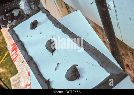 Installation einer weißen Polystyrol-Wärmedämmung, Detail auf grauem Klebezementkleber auf weißen Platten Stockfoto