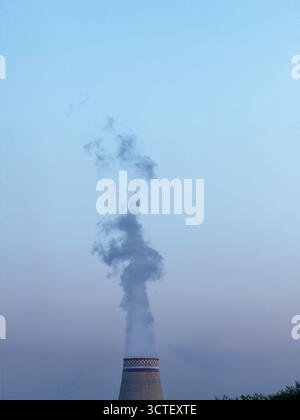 Der industrielle Kühlturm lässt die Wolke in den blauen Abendhimmel und die dramatische Stimmung in der Industrielandschaft frei Stockfoto