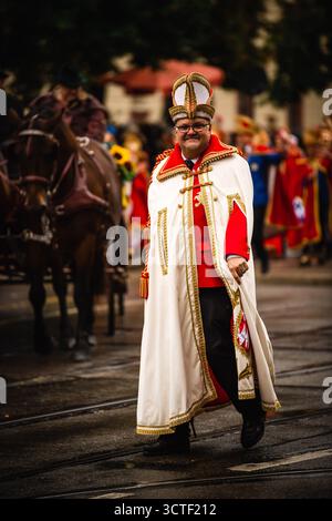 München, Deutschland - 18. September 2022: Blick auf einen Mann in traditioneller Kleidung, mit weißem Mantel und verziertem Hut, bei der Oktoberfestparade in der Nähe der belebten Straßen. Stockfoto