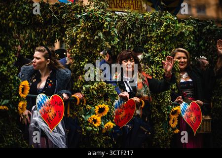 München, Deutschland - 18. September 2022: Blick auf Frauen in traditioneller Kleidung, die bei der temperamentvollen Oktoberfestparade zwischen leuchtendem Grün und Sonnenblumenakzenten winken. Stockfoto