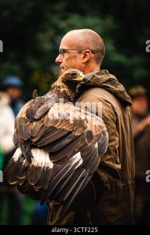 München, Deutschland - 18. September 2022: Blick auf einen Mann mit einem majestätischen Goldadler während der lebhaften Oktoberfestparade, dessen braune und goldene Federn sich von seiner beigefarbenen Jacke abheben. Stockfoto