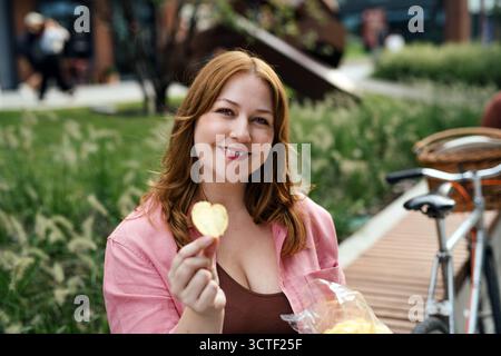 Eine Frau mit Kartoffelchips in der Hand, die draußen sitzt. Stockfoto