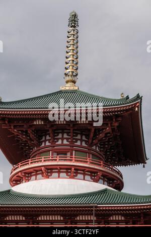 Der Blick auf die markante rote Pagode mit ihren gestuften Dächern und dem goldenen Turm reicht bis zum bewölkten Himmel, einem architektonischen Wunder, Narita, Chiba, Japan. Stockfoto
