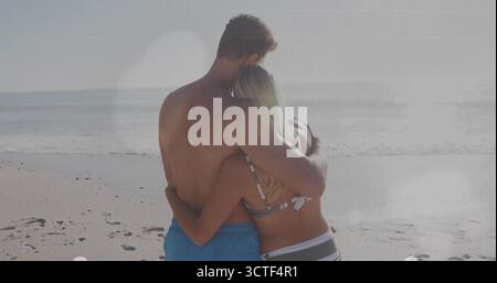 Umarmtes Paar in gestreiften Bikinis und blauen Badehosen, das ruhige Meer inmitten von Sandstrandabdrücken blickt Stockfoto