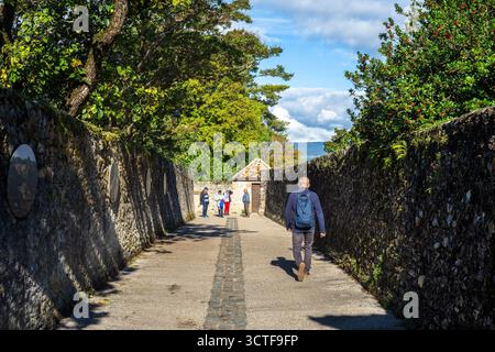 Yvoire, Frankreich - 25. September 2025: Eine Person, die einen Steinweg im mittelalterlichen Yvoire entlang geht, umgeben von hohen Steinmauern und Bäumen, mit einer Gruppe von p Stockfoto
