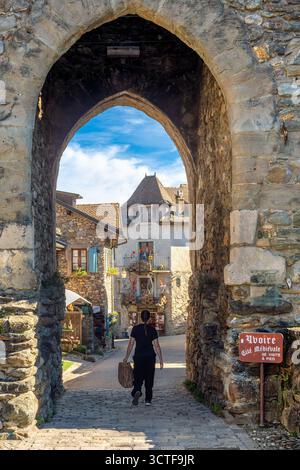 Yvoire, Frankreich - 25. September 2025: Eine Person geht durch einen mittelalterlichen Steinbogen in ein malerisches Dorf Yvoire mit Kopfsteinpflasterstraßen und Straßen Stockfoto