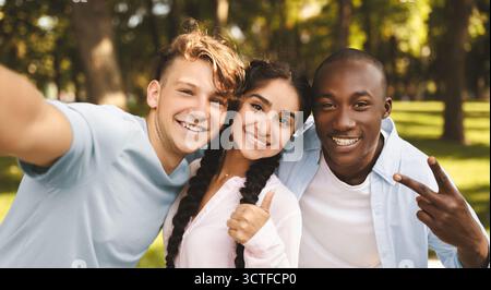 Multirassische Studenten befreunden sich, Selfie zu machen, V-Zeichen zu gestikulieren und Daumen hochzuzeigen, im Freien auf dem Campus zu posieren Stockfoto