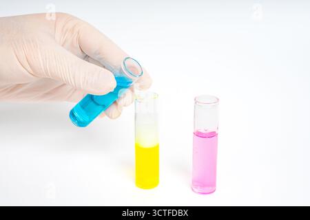Hände mit Handschuhen, die Glasröhrchen mit blauen, rosa und gelben Flüssigkeiten auf isoliertem weißen Hintergrund halten. Farbenfrohe wissenschaftliche Experimente. Chemische Reaktion Stockfoto