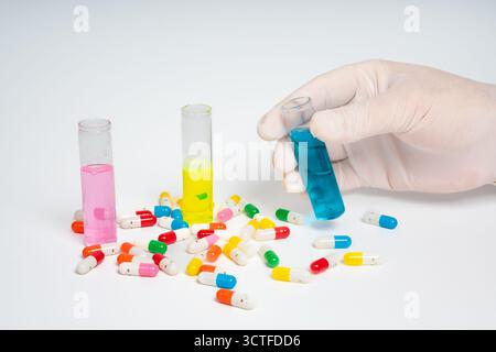 Handschuhe halten Reagenzglas mit blauer Flüssigkeit, bunte Pillen isoliert auf weißem Hintergrund. Glasröhrchen und Pillen in Hand gehalten Stockfoto