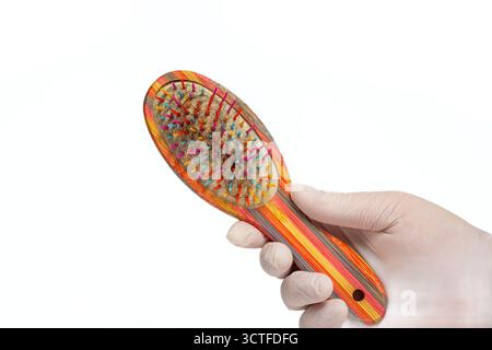 Hand mit Handschuhen, die bunte Haarbürste mit losen Haarsträhnen in Borsten auf isoliertem weißem Hintergrund hält. Pflege, Pflegeprobleme Stockfoto